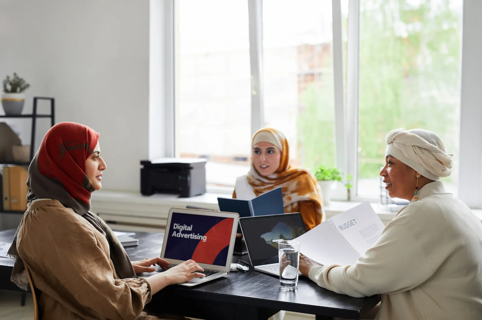 Three businesswomen in a meeting room discussing digital advertising projects.